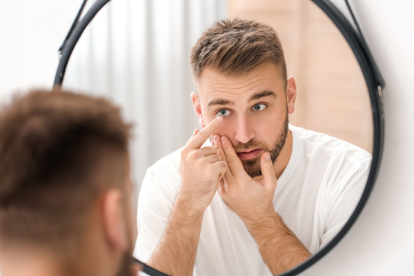A man looks into the mirror to insert a contact lens into his eye