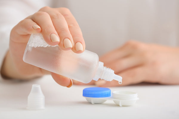 A woman places saline solution into her contact lens case to rinse her lenses before insertion